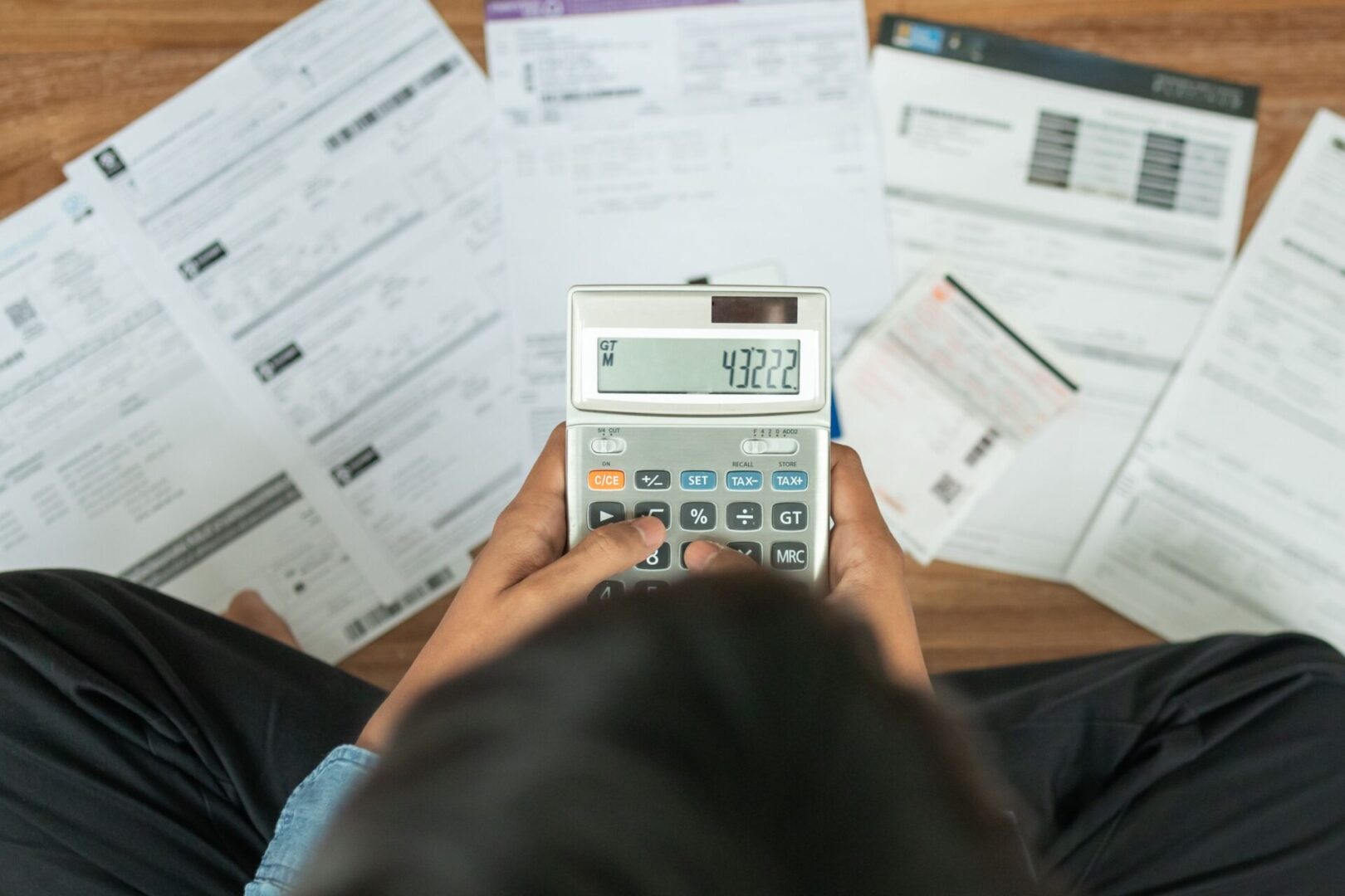 A person holding an electronic calculator in front of papers.